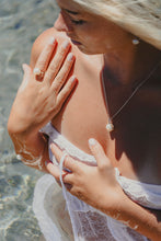 Woman in a white dress with pearl jewelry standing in shallow water.