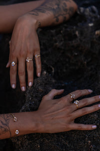 Close-up of the model’s hands resting on a dark rock background, showcasing Higher Realm Herkimer Diamond rings in gold, paired with a matching bangle.