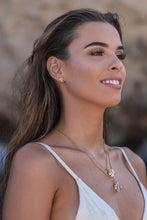 Close-up of the model wearing two Higher Realm Herkimer Diamond Crystal Necklaces in gold, paired with matching gold Herkimer Diamond stud earrings, set against a blurred rocky backdrop, highlighting the clarity and brilliance of the Herkimer diamonds.