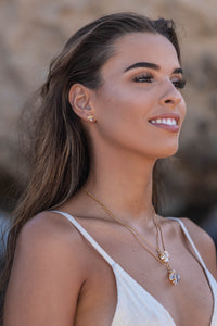 Close-up of the model wearing two Higher Realm Herkimer Diamond Crystal Necklaces in gold, paired with matching gold Herkimer Diamond stud earrings, set against a blurred rocky backdrop, highlighting the clarity and brilliance of the Herkimer diamonds.