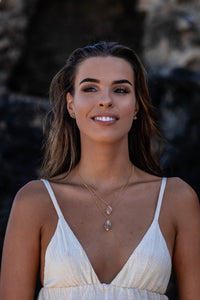 Front-on shot of the model wearing two Higher Realm Herkimer Diamond Crystal Necklaces in gold, with a blurred rocky backdrop, emphasising the elegance and shine of the Herkimer diamonds.