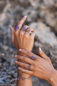 Extreme close-up of the model wearing all sizes of the Violet Horizon Amethyst crystal rings in gold, paired with a matching amethyst bangle, highlighting the intricate details of the raw crystals.