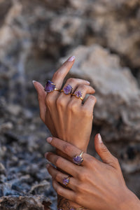 Extreme close-up of the model’s hands adorned with five Violet Horizon Amethyst crystal rings in gold, highlighting the raw beauty and intricate details of the crystals.