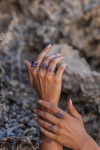 Model’s hands adorned with Violet Horizon Amethyst crystal rings in gold, set against a rocky backdrop, showcasing the deep purple hues of the amethyst stones.