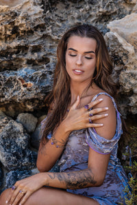 Model sitting against a rocky backdrop, elegantly displaying Violet Horizon Amethyst crystal rings in her hand, highlighting their raw beauty.