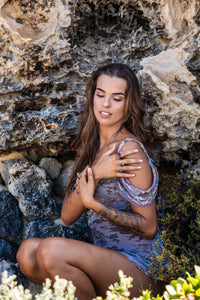 Model sitting against a rocky backdrop, holding Violet Horizon Amethyst crystal rings in her hand, captured from a wider angle to showcase the scene.