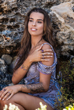 Model sitting against a rocky backdrop, showcasing Violet Horizon Amethyst crystal rings in all sizes, emphasising the natural beauty of the amethyst stones.