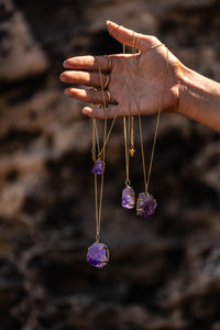 Model holding Violet Horizon Amethyst crystal necklaces draped over her hands, with all sized amethyst stones, set against a rocky background.