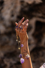 Model’s hand holding all four sizes of Violet Horizon Amethyst crystal necklaces in gold, draped over her hand, showcasing the Blackwood Ave logo. She is also wearing three sizes of amethyst rings.