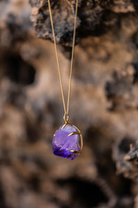 Close-up of a Violet Horizon Amethyst crystal necklace with amethyst stones draped over a rocky surface, creating a natural, textured backdrop.