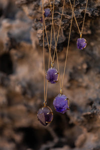 All four sizes of the Violet Horizon Amethyst Crystal Necklace in gold, elegantly draped over rugged rocks, with the camera focused on the raw amethyst stones.