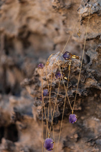 Violet Horizon Amethyst crystal necklaces draped over rocks, accompanied by several amethyst rings, creating a natural, earthy display.