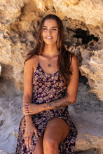 Model sitting against a rocky backdrop, wearing the Twilight Veil Amethyst Crystal Cluster Necklace, amethyst rings, and a matching bangle, showcasing the natural elegance of the pieces.