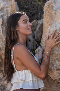 Model wearing Higher Realm Herkimer Diamond rings, bangle, and thread earrings in gold, standing against a sandy rock formation backdrop, showcasing the elegant sparkle of the diamonds in natural light.