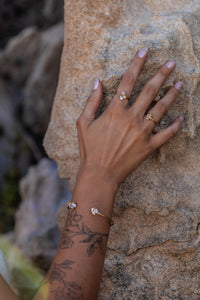 Model’s hand on a sandy rock formation showcasing two small Higher Realm Herkimer Diamond rings in gold, paired with the matching Herkimer Diamond bangle, highlighting the clarity and elegance of the Herkimer diamonds.