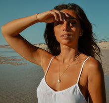 Model wearing the Freshwater Pearl Necklace in gold with the lagoon behind her.